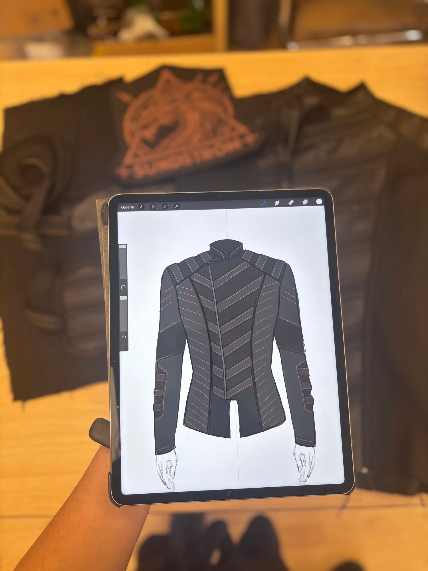 A black leather jacket on a workbench with its digital pattern drawing open on a tablet