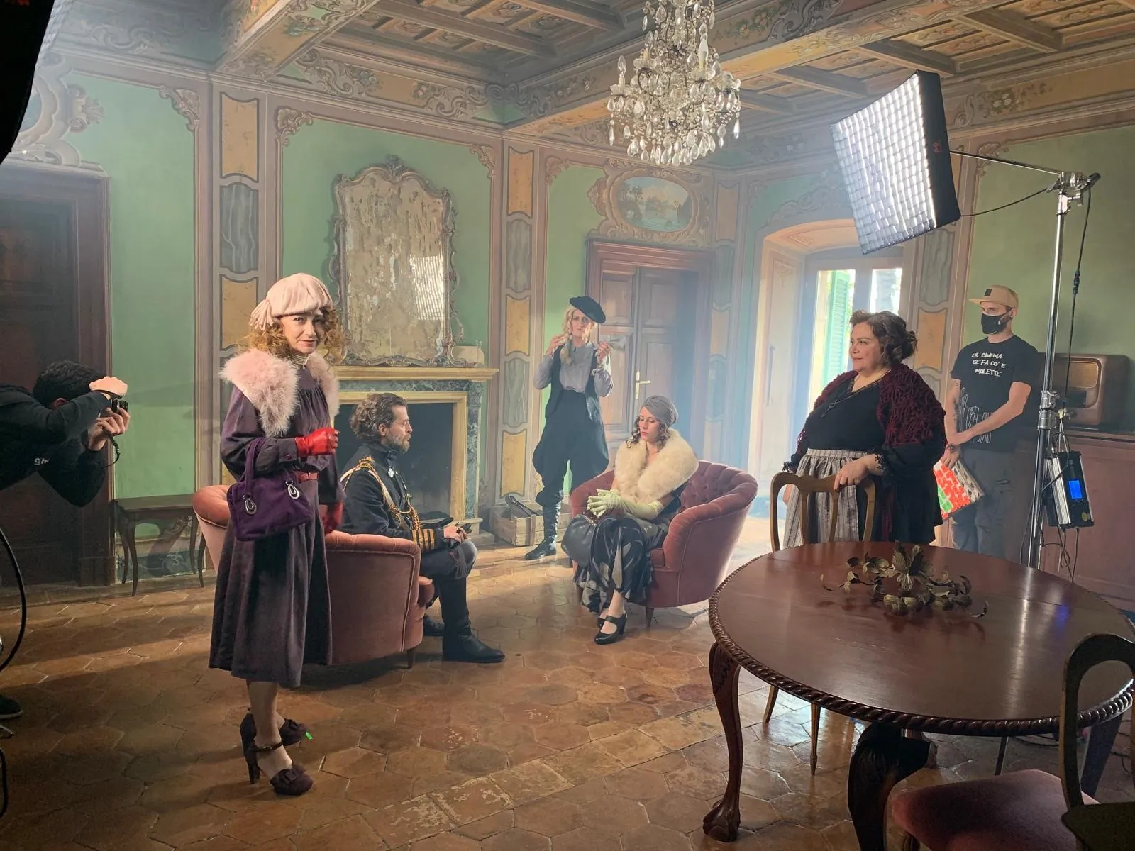 A film set in a green period room with actors and crew